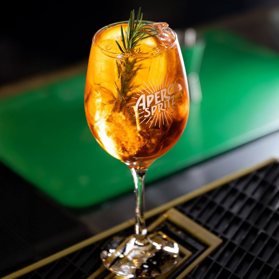 Taça de Aperol Spritz com laranja e alecrim no balcão do bar