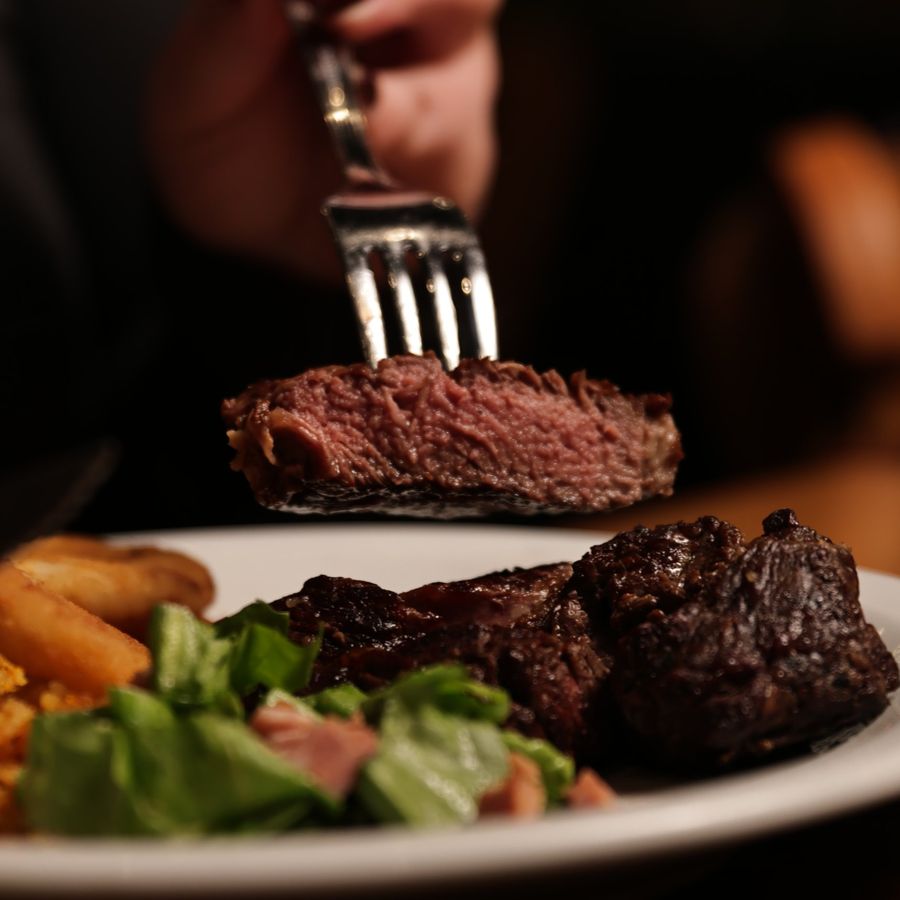 Pedaço de carne no garfo sobre o prato, com salada e batatas