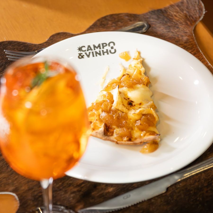 Fatia de pizza no prato do Campo & Vinho, com uma taça de Aperol Spritz em primeiro plano