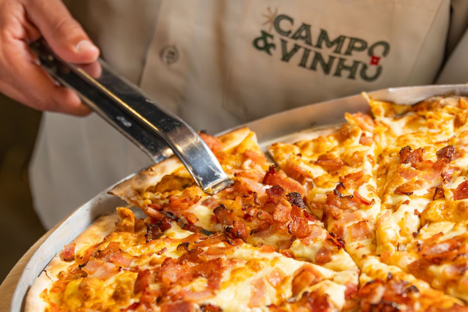 Garçom do Campo & Vinho serve uma fatia de pizza no rodízio